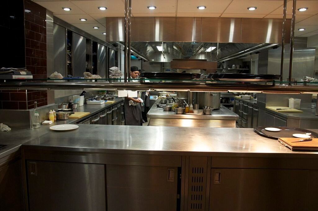 Professional restaurant kitchen with stainless-steel benches, cooking equipment and food-preparation areas.