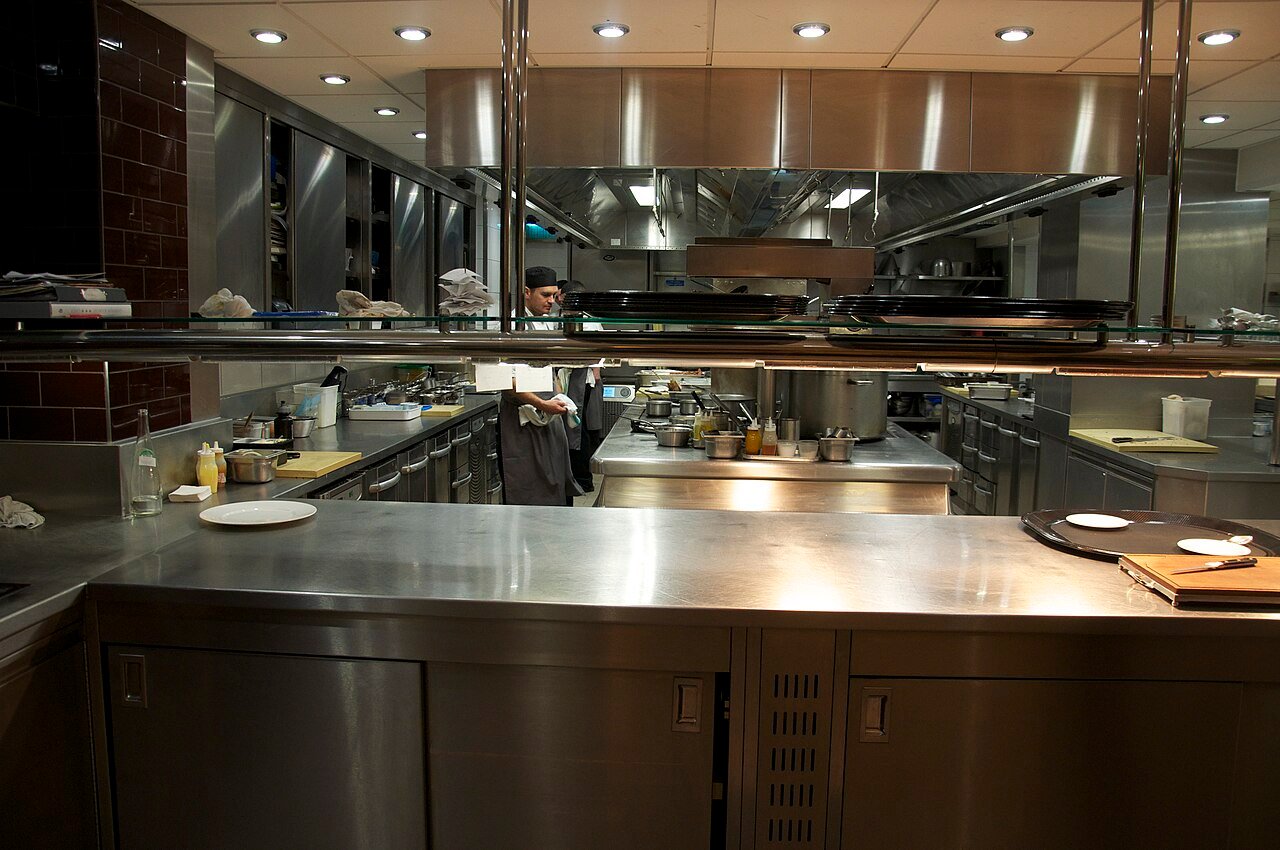 Professional restaurant kitchen with stainless-steel benches, cooking equipment and food-preparation areas.