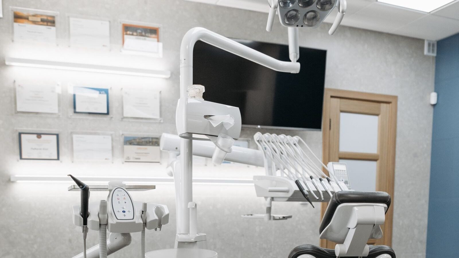 Empty modern dental treatment room with dental chair, overhead light and surrounding clinical surfaces.